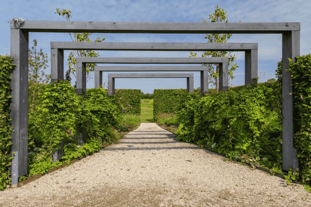 Geradliniger Gartenweg mit aufeinanderfolgenden Holzrahmen, der den Blick durch eine Öffnung in die umliegende Landschaft lenkt