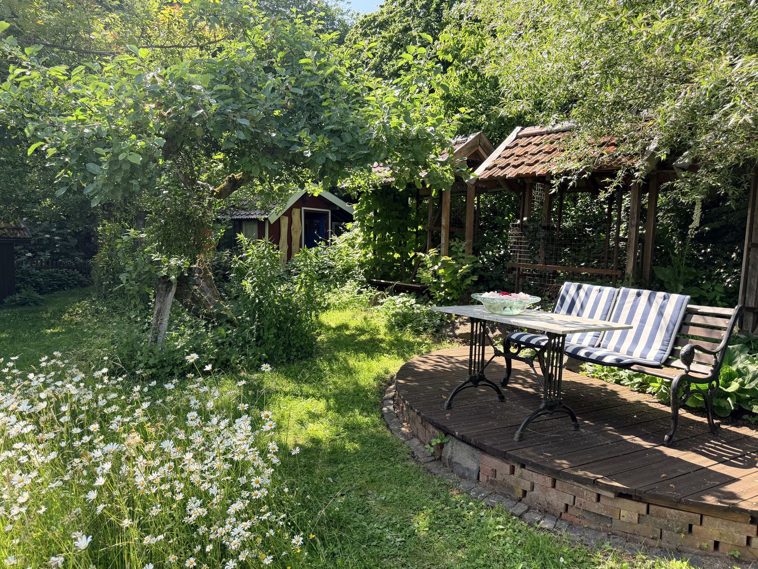 Rundes Holzdeck mit Gartenbank und Tisch zwischen blühenden Wieseninseln