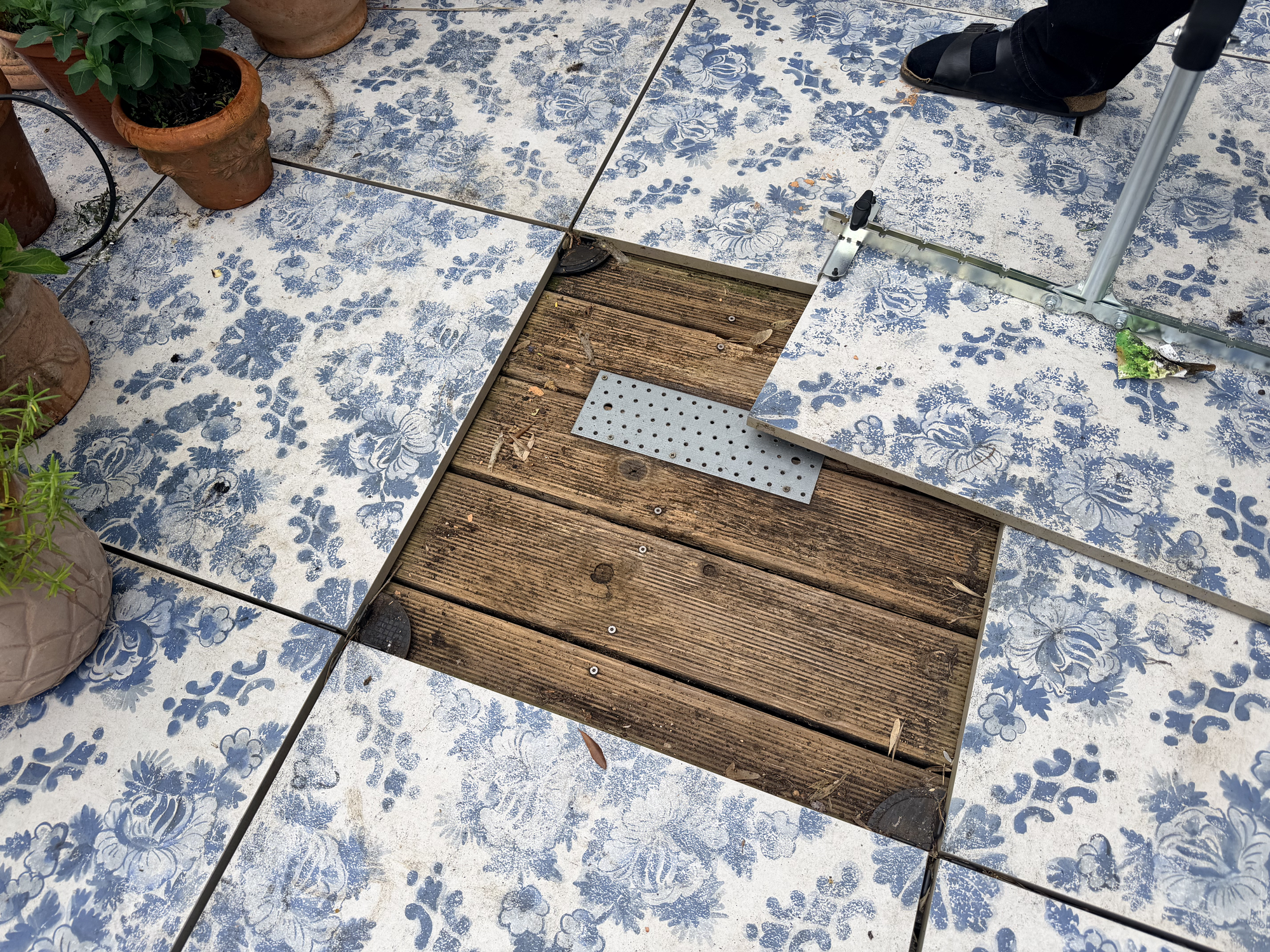 Blau-weiße Terrassenfliesen auf Stelzlagern, eine Platte hochgenommen